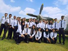 a group of people standing next to each other in front of an airplane on the grass