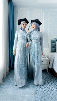 two women in blue gowns standing next to each other with an umbrella over their heads