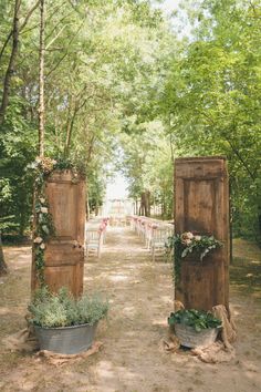 an outdoor ceremony set up with wooden doors and flower pots on the ground, surrounded by greenery