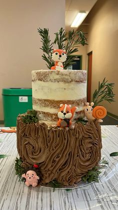 a three tiered cake with frosting and woodland animals on the top is sitting on a table