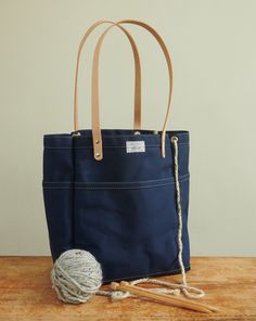 a blue tote bag sitting on top of a wooden table next to knitting needles