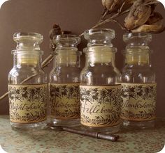 four glass bottles with labels on them sitting on a table next to a dried plant