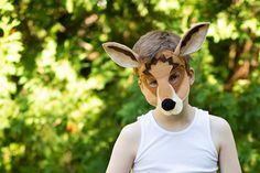 a young boy wearing a deer mask with trees in the background