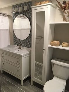 a white toilet sitting next to a sink in a bathroom under a large round mirror