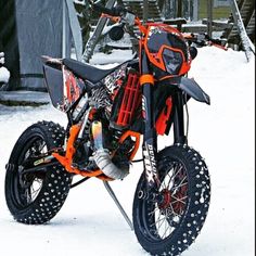 an orange and black dirt bike parked in the middle of some snow covered yard area