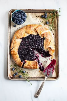 a blueberry pie on a baking sheet with berries around it