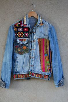 a denim jacket with colorful patches and beads hanging on a hanger in front of a wall