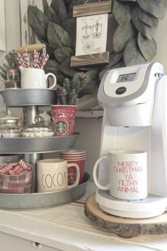 a coffee maker sitting on top of a counter next to cups and mugs in front of a christmas wreath