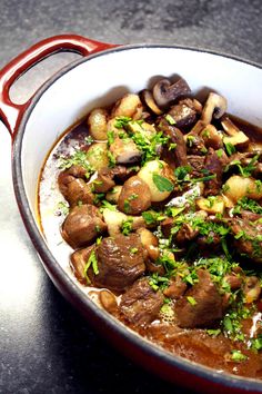 a red pot filled with meat and mushrooms