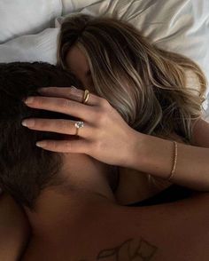 a woman laying on top of a bed with her arm around a man's head