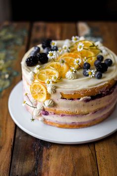 a cake with fruit and flowers on it sitting on a table next to a plate