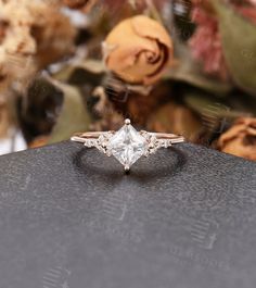 an engagement ring sitting on top of a black piece of cloth with flowers in the background