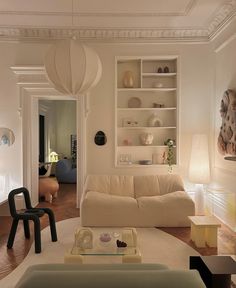 a living room filled with white furniture and lots of shelves next to a doorway that leads to another room