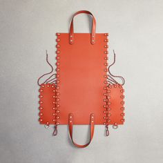 an orange leather bag with rivets on the handles and straps, hanging from a hook