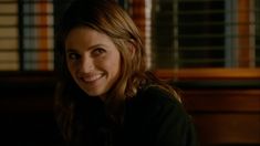 a smiling woman with long brown hair sitting in front of a wooden table and looking at the camera