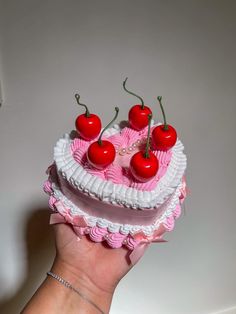 a hand holding a pink and white cake with cherries on top