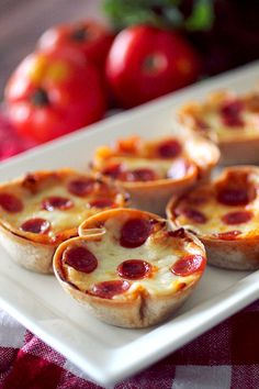 mini pizzas on a white plate with tomatoes in the backgroung behind them