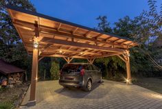 a car is parked under a wooden covered carport in a driveway at night with lights on