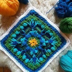 a crocheted square with blue, green and yellow flowers on it next to balls of yarn