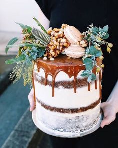 someone holding a cake decorated with nuts and greenery on the top, in front of an instagram photo