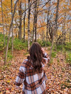 a woman standing in the woods with her back to the camera, looking at trees and leaves