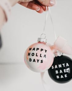 a person holding two ornaments that say happy holla days and santa bae bake