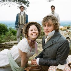 two people dressed in period clothing sitting on the ground next to each other and one person wearing a hat