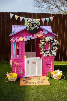 a pink toy house sitting on top of a lush green field next to a wooden fence