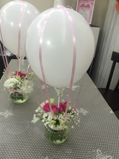 three white balloons with pink ribbons are sitting on a table in front of flowers and vases