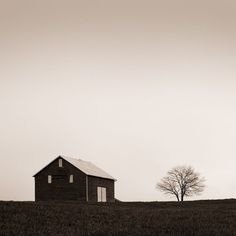 black and white photograph of an old barn on a hill with a lone tree in the foreground