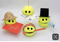 three tennis balls with faces and hats on them, each holding an orange pencil in their mouth