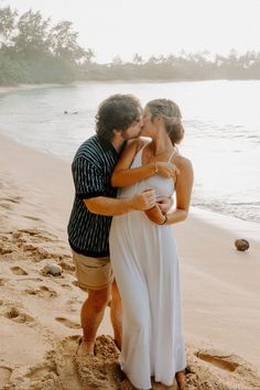 a man and woman kissing on the beach with water in the backgrouund