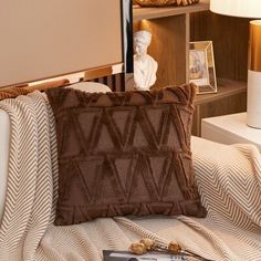 a brown pillow sitting on top of a bed next to a white lamp and book