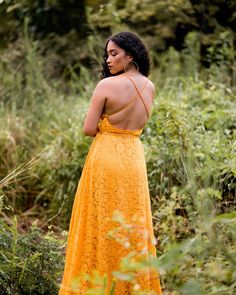 a woman in an orange dress is standing in tall grass with her back to the camera