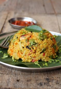 a plate filled with rice and vegetables on top of a leafy green tablecloth