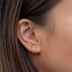 a close up of a woman's ear with two small gold hoop earrings on it