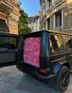 a black jeep with pink flowers in the back door is parked next to a building