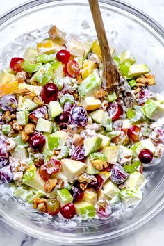 a glass bowl filled with fruit salad and topped with walnuts, apples, celery, cranberries