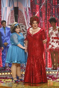 two women dressed in red and blue standing next to each other on the stage with one holding her hand out