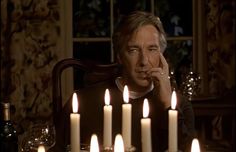 a man sitting at a table with many lit candles in front of him and his hand to his face