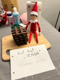 an elf is sitting on top of a cutting board next to a sign that says kit kat lenga