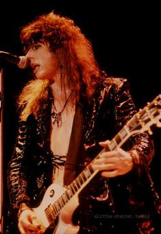 a man with long hair playing an electric guitar in front of a microphone on stage