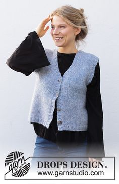 a woman standing in front of a white wall wearing a gray vest and black shirt