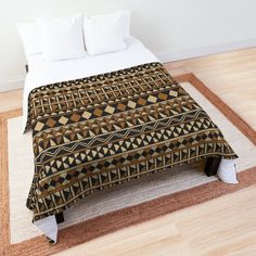 a bed covered in a brown and black blanket on top of a wooden floor next to a white pillow