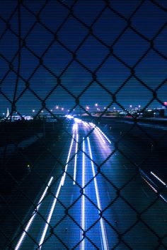 the view from behind a chain link fence at night, looking down an empty highway