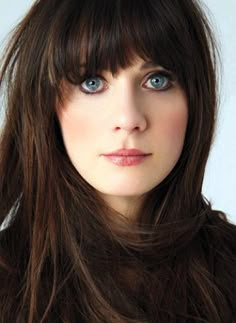 a woman with long brown hair and blue eyes is looking at the camera while she has bangs