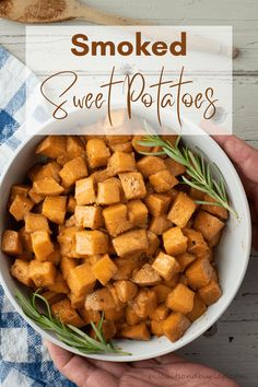 two hands holding a white bowl filled with cooked sweet potatoes and rosemary sprigs