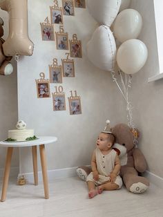 a baby is sitting on the floor in front of some balloons and pictures hanging from the wall