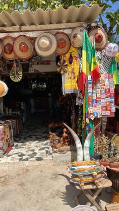 an outdoor market with lots of hats hanging from it's roof and various items on display