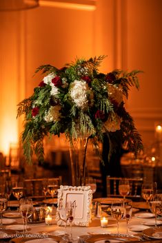 a tall centerpiece with flowers and greenery sits on a table set for dinner